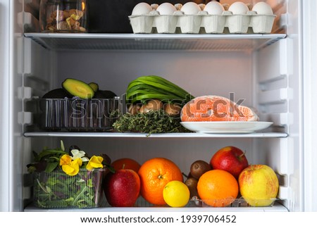 Open fridge with healthy food.Products on the shelves.Proper nutrition with red fish, avocado and fruits.Refrigerator with healthy products.Fruits, eggs, fish, avocado, mushrooms, herbs, kiwi, orange.