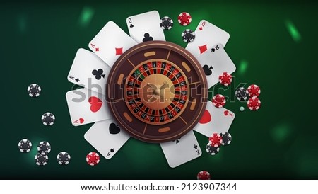 Casino roulette on green table with poker chips and playing cards, top view. Background for your arts