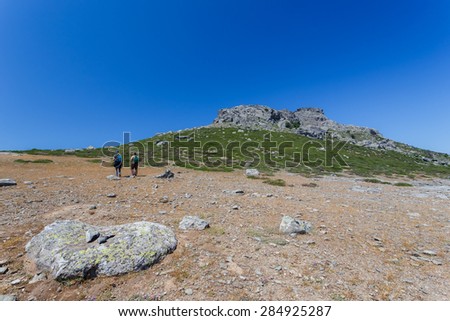 A pair of climbers or strollers walking up the mountain with backpacks against a blue sky
