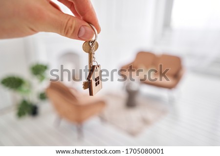 Men hand holding key with house shaped keychain. Modern light lobby interior. Mortgage concept. Real estate, moving home or renting property.