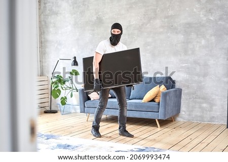 Thief with black balaclava stealing modern expensive television. Masked face. Man burglar stealing tv set from house Foto stock © 
