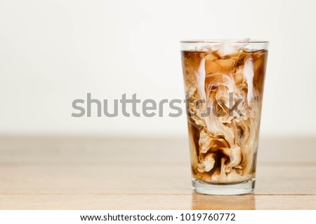 Ice coffee on a wood table with cream being poured into it showing the texture and refreshing look of the drink, with a clean background.