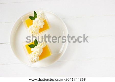 Orange Panna cotta  , delicious italian dessert with whiped cream, portion dessert in a clear plastic cups. White wooden board, healthy eating , healthy dessert, italian dessert background