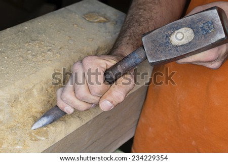 A stonemason working a large stone block of sandstone with a hammer and chisel