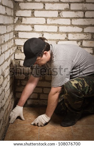 Builder setting ceramic tile on cement floor