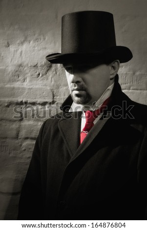 Man in the black coat, top hat and in a red tie on a wall background