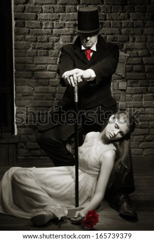 Man in the black coat, top hat and in a red tie and beautiful girl with rose