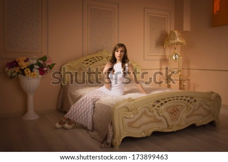 Elegant girl in evening dress posing in an elegant bedroom