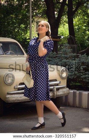 Beautiful lady in vintage dress standing near retro car