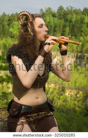 Pretty female faun in a wood. Woman with a mythological creature playing flute