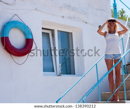 A beautiful young blond woman lifeguard watching through binoculars at the rescue station.