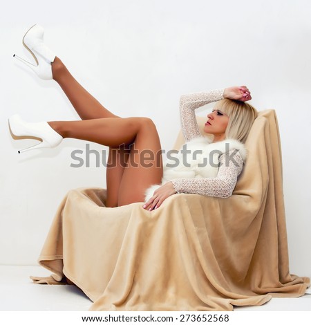 Beautiful sexy blonde with long legs in shoes with heels lying on a chair