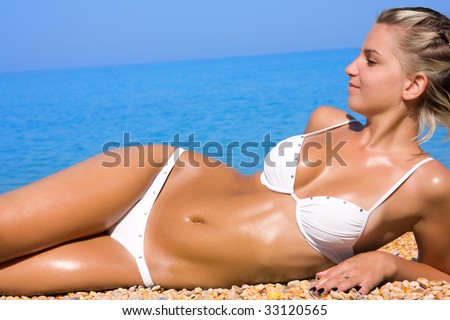 The young blonde girl with a beautiful body sunbathes on a beach in a white bathing suit against the sea