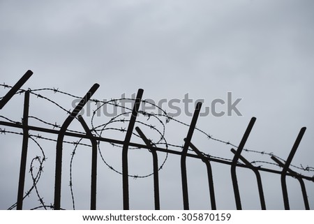 Old barbed wire fence in silhouette fencing an industrial site