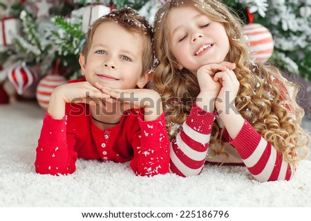 Happy brother and sister are playing on the floor near Christmas tree. little friends enjoying New Year party, Christmastime holidays, best friends, happiness concept