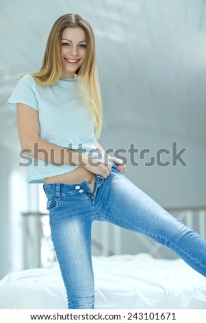 Woman dressed. Young blond hair woman lying on the bed and pulling on skinny jeans