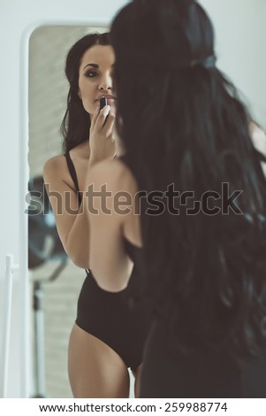 fashion interior photo of beautiful sensual woman with dark hair doing makeup in makeup room,looking at the mirror