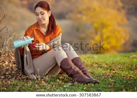 Beautiful woman relaxing and drinking coffee, sitting in autumn garden, wrapped in a blanket wool blanket.
