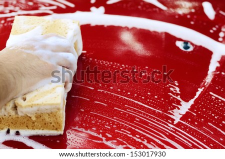 Human arm with sponge soap washing red car surface