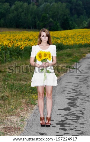 Young woman in white short dress with sunflowers at country road