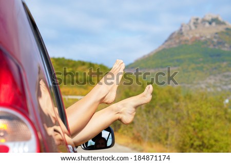 Female bare feet stick out of car window on mountain background. Travel concept.