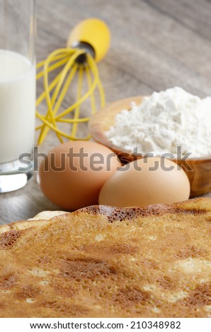 Milk, flour, whisk, pancakes and eggs on wooden table