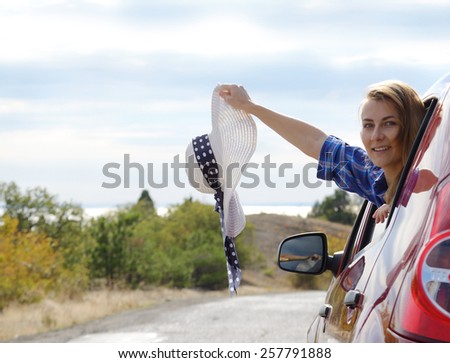 Young happy woman holds sun hat looking from car window