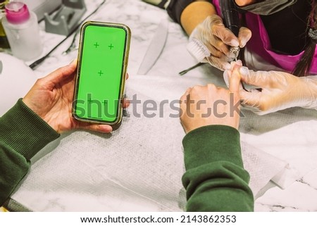 Women's hands in the manicure process close-up. Self-care at the beauty salon. Hand nail treatment by hardware. The client looks into the screen of the smartphone. Phone Screen Mockup