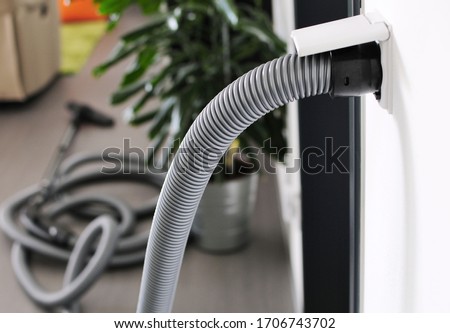 Closeup of central vacuum cleaner hose plugged in to wall inlet socket. View in to room with central vacuum cleaner.