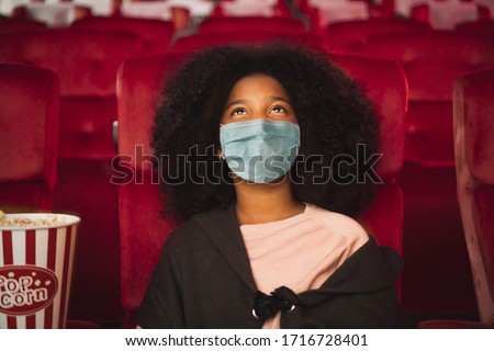 Happy african kid wearing protective face mask and watching movie in theater/theatre cinema protect infection from coronavirus covid-19, social distancing in theater concept
