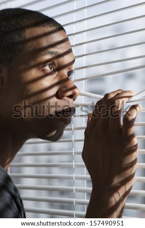 Young, nervous black man looking out window, vertical