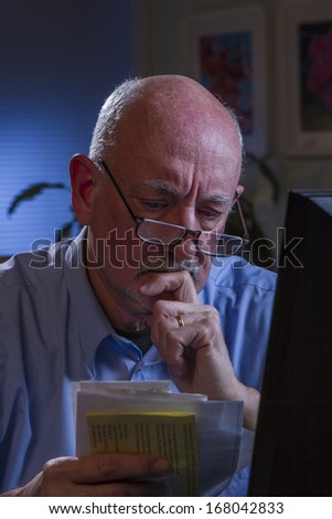 Distressed older man at computer and looking through bills, vertical