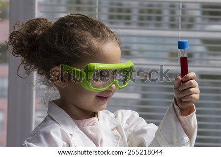 female child in lab coat with test tube and safety goggles.