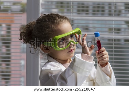 female child in lab coat with test tube and safety goggles.