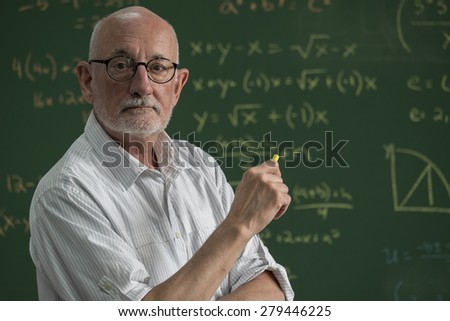 Older male teacher standing in front of a chalkboard in a classroom