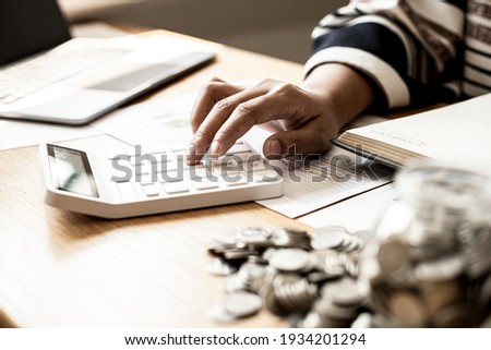 A woman is pressing a calculator to calculate expenses, she is doing an income-expense account and a money-saving plan to buy funds to make her money grow. Money saving ideas for investment