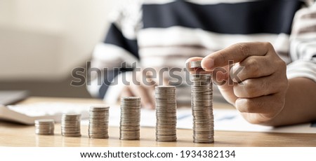 Women are stacking coins on top of the coin pile on the highest row. Placing coins in a row from low to high is comparable to saving money to grow more. Money saving ideas for investing in funds.