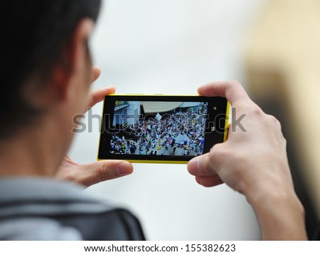 BANGKOK - JUN 30: A passerby uses a smartphone to capture an anti-government rally on Jun 30, 2013 in Bangkok, Thailand. The protesters known as V for Thailand call for the government to be removed.