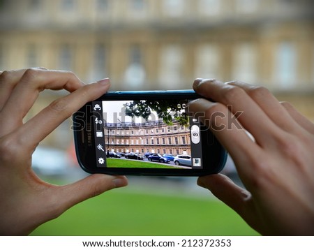 BATH - AUG 9: A tourist uses a smartphone to capture a local landmark on Aug 9, 2014 in Bath, UK. A popular travel destination and UNESCO world heritage city, Bath receives 4.5mn visitors annually.