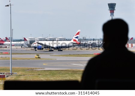 LONDON - JUN 17: A traveler watches airplanes taxi on tarmac at Heahrow Airport on Jun 17, 2015 in London, UK. Heathrow is one of the world\'s busiest airports handling 73.4 million passengers in 2014.