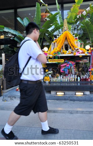 BANGKOK - JUNE 9: Unidentified Thai student wais a spirit house as he walks past on June 9, 2010 in Bangkok, Thailand. It is customary for Thais to wai or leave offerings at spirit houses.