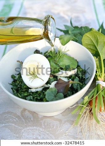 Healthy enrich salad with spring native-grasses weed and vegetable plants, arranged with boiled eggs in a white bowl on table-cloth decorated with a bunch of weed herbs