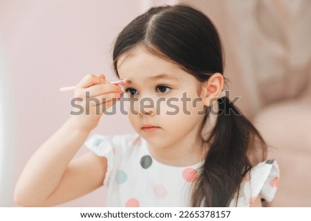 a beautiful little girl in the mirror preening. a little girl is sitting at a children's table and is wearing children's cosmetics. Foto stock © 