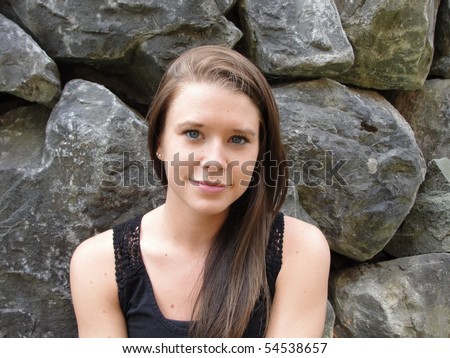 Blue eyed brunette female young woman slight smile in a black tank top against a rock wall
