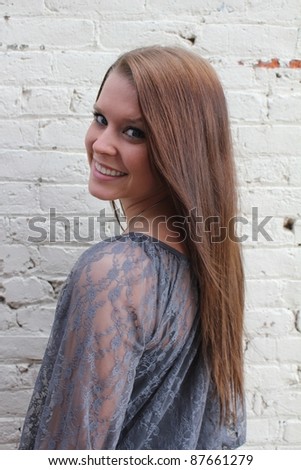 Young woman with long brown hair looks back over her shoulder with a smile