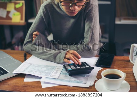 Season to pay Tax and Budget planning concept. Business woman calculating annual tax and using mobile phone. Calendar 2021 and personal income tax form placed on home office desk.