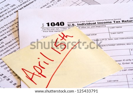 Tax Day Reminder - A 1040 tax form and a reminder note with April 15th written on it. The corner of the note is hiding the date to add to the image usefulness.