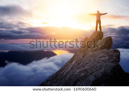 Adventurous Man Hiker With Hands Up on top of a Steep Rocky Cliff. Sunset or Sunrise. Landscape Taken from British Columbia, Canada. Concept: Adventure, Explore, Hike, Lifestyle. Composite. 