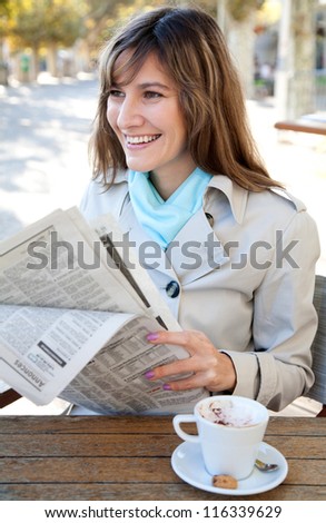 Cheerful woman reading newspaper in the outdoor cafe