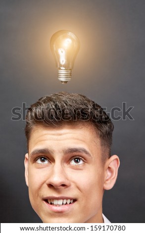 Head of young man looking up at bulb light over black background